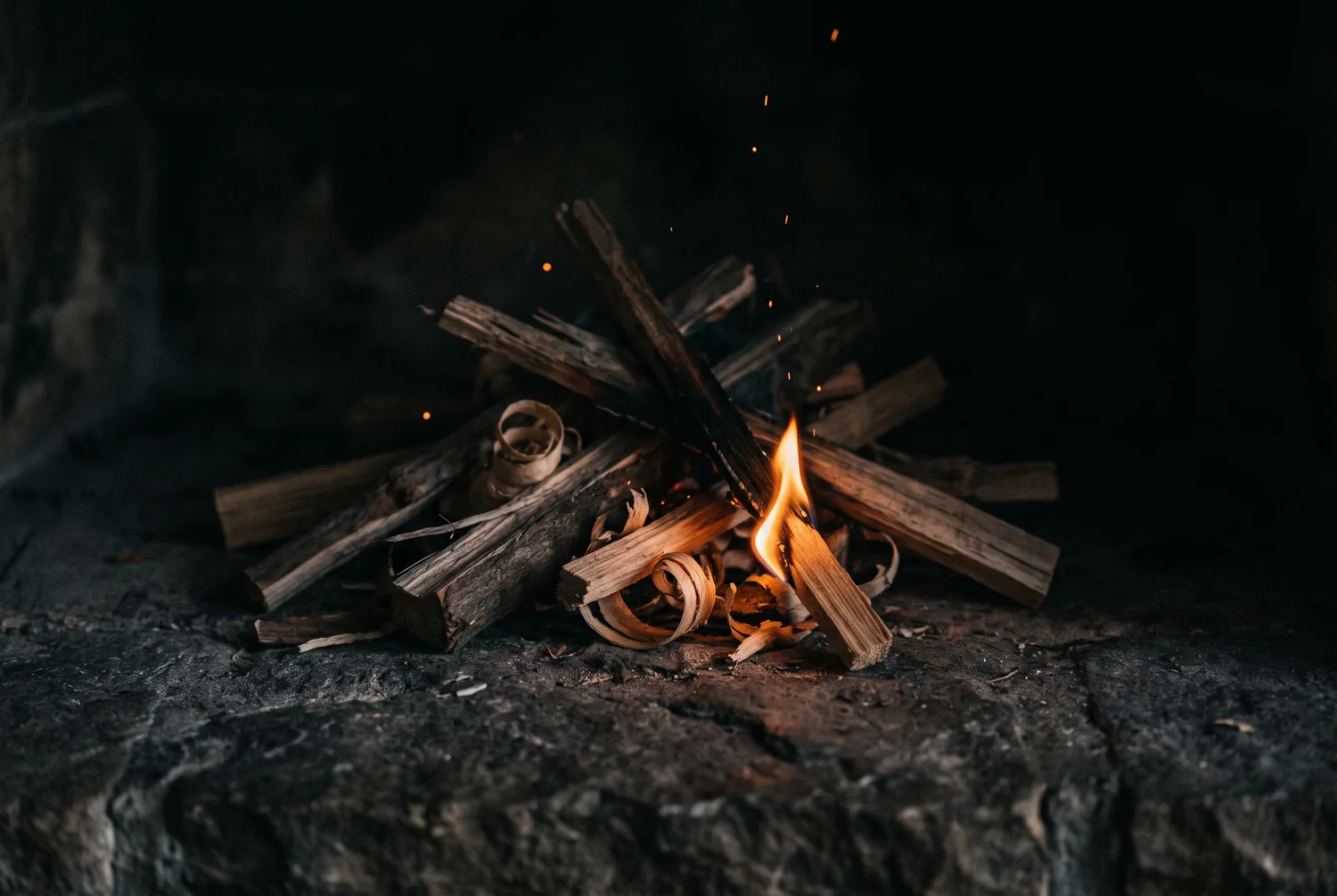 Trockenes Anzündholz fängt Feuer auf einem dunklen Steinherd